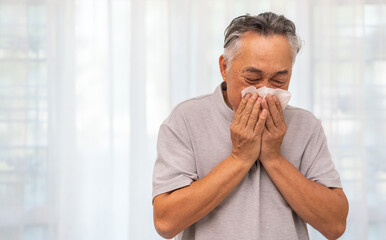 Senior asian man sneezing into a tissue, experiencing discomfort from cold or allergies, seasonal allergies, virus, flu and sick health, wellness, senior care, and medical treatment for respiratory.