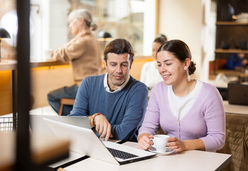 Confident male and female cafe customer enjoying coffee while working on laptop