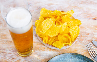 Crispy potato chips with glass of cold beer served on table.