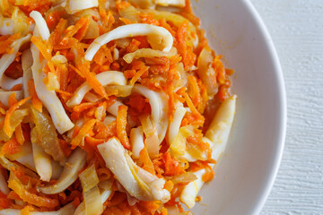 Stir-fried Squid with onions, carrots in a spicy sauce on white plate close up, top view