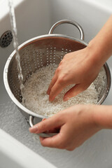 Woman rinsing rice in colander at sink, closeup