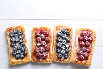 Tasty puff pastries with berries on white wooden table, flat lay. Space for text
