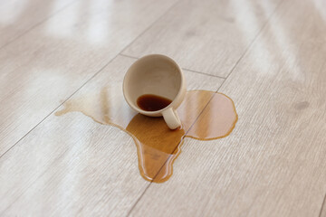 Cup with spilled drink on wooden floor, closeup