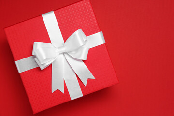 Gift box with white bow on red background, top view. Space for text