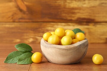 Ripe plums in bowl and leaves on wooden table