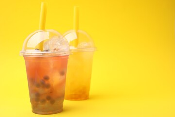 Tasty bubble tea in plastic cups on yellow background, space for text