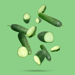 Many ripe cucumbers falling on green background