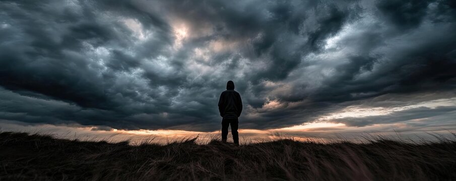 A silhouetted figure stands against a dramatic sky filled with dark clouds and a hint of light, evoking a sense of wonder and introspection.
