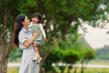 mother holding and comforting her crying toddler baby girl on grass field in park