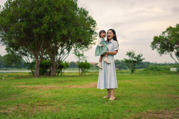 happy mother holding and laughing with toddler baby girl on grass field in park