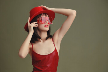 A woman in a red hat and sunglasses poses confidently, one hand resting on her head and the other...