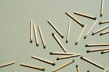 Wooden matchsticks with green tips scattered on light green surface.