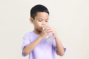 cute little asian boy Standing and Smiling little with a holding an empty glass of water on white background.