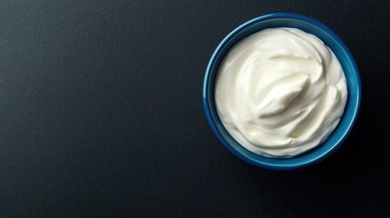 Creamy yogurt in a vibrant blue bowl on a textured dark surface, showcasing its smooth texture and rich color, perfect for dips or adding to dishes.