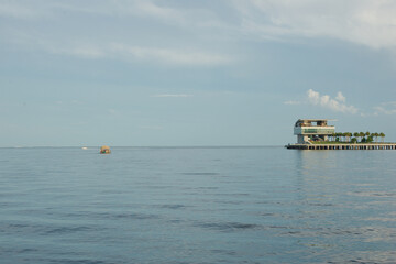 Wide shot Looking  south over green grass, palm trees, seawall and sandy beach St. Petersburg, FL. towards Tampa Bay and Pier in back. Partly sunny day with blue sky, gray and white clouds. Reflection