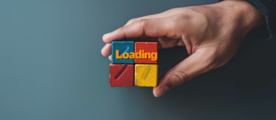 Hand holding colorful block with text "Loading" on grey background. Loading screen concept for web design and mobile app development.