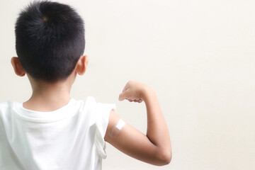 Little asian child boy with bandage plaster on her arm after Covid-19 vaccination. Injection covid vaccine, healthcare for children.