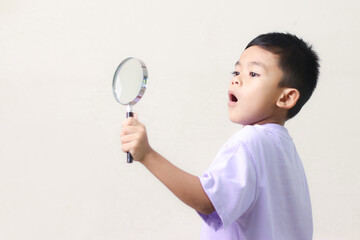 Portrait of surprised cute little asian boy looking through a magnifying glass. Education concept.