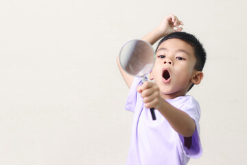 Portrait of surprised cute little asian boy looking through a magnifying glass. Education concept.