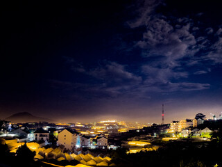 evening landscape along the hillside of the city, agricultural greenhouses tower lights up, cloudy sky