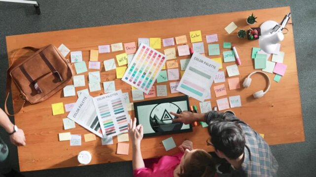 Top view of smart designer holding color palette while project manager looking at design and choosing color for program. Professional businesswoman taking a note while design creative logo. Symposium.