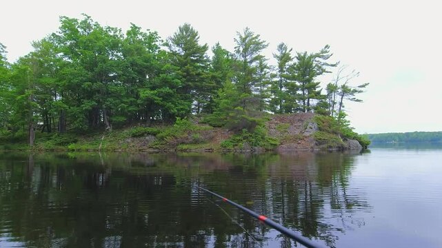 Angler casting rod with artificial baitfish lure for big mouth bass in the early morning, while trolling on inflatable dinghy boat. Fisherman hand holding tackles with lake nature on the background.