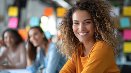 Fototapeta premium Group of smiling diverse women in a modern office setting with colorful sticky notes on the wall. Business teamwork concept.