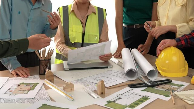 Smart architect and safety engineer discussion about building blueprint on table with architectural document, measurement tools and wooden block scatter around at modern office. Closeup. Delineation.