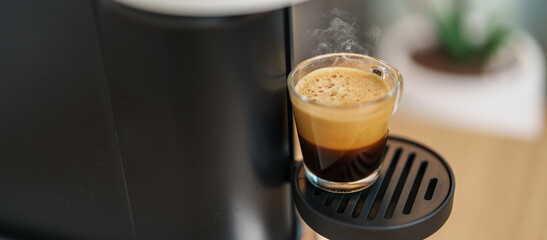 Espresso cup with steam and froth during Coffee making Coffee by Coffee Maker Machine on wood table bar. Cafe shop, Daily beverage drink at Home, Apartment and Office concept