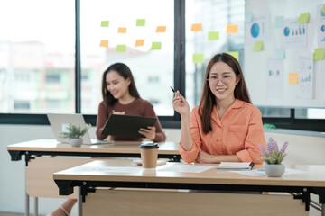 Two women sitting at desks with a white board behind them