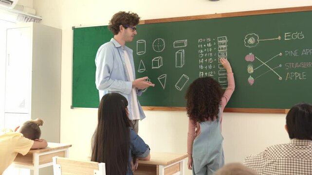 Back view of african student answer question while writing at board. Teacher looking at elementary student doing math quiz in front of classroom while smart children attend in math lesson. Pedagogy.