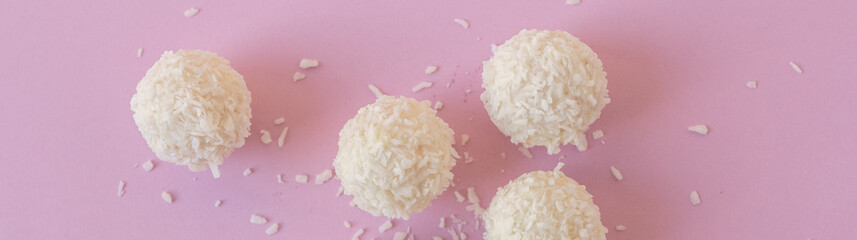 Top view of White Chocolate Candy With Coconut Topping over pink background, sweet balls flat lay banner
