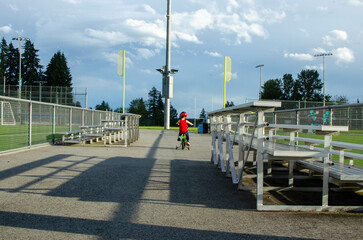 Child Riding a Bicycle at a Park Near Sports Fields and Bleachers on a Sunny Day