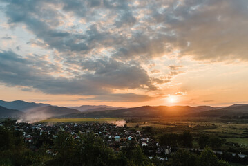 Sunset over village in spring. Rural landscape with fields, and mountains. Photo for the background with a view of the village and sunlight.