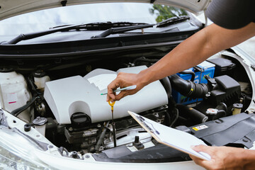 A technician in a Thailand auto repair shop conducts diagnostics on a car engine using a laptop....