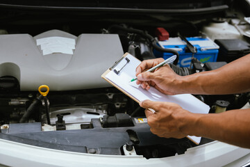 A technician in a Thailand auto repair shop conducts diagnostics on a car engine using a laptop. The scene highlights advanced technology in automotive inspection and repair.