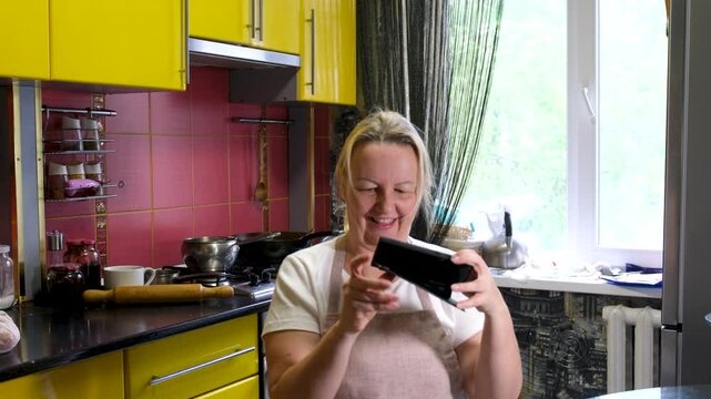 fight for a mobile phone woman comes up takes the game from her husband sits down to play herself. wife hits husband with towel. adult woman housewife apron home conditions