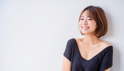 Obraz premium A portrait of a teenage Japanese woman with short hair, wearing black clothing, smiling against a white wall background.