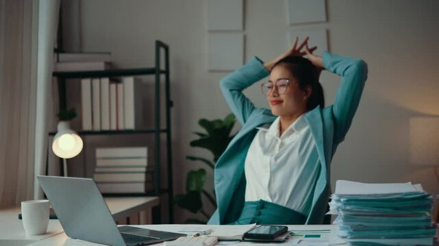 Asian accountant woman taking a break in her office, stretching and relaxing after a long session of working on her laptop, showcasing a moment of well-deserved downtime