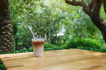A glass of iced latte coffee on wooden table in the garden