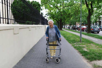Beautiful elderly woman walking on city street with rollator, going shopping to the store.