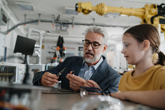Father and girl during kid at work day, encouraging girl in career in robotics. Teacher showing young schoolgirl how to assemble small robot. - Powered by Adobe
