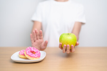 woman hand hold green Apple and reject donut, female fitness choose between fruit is Healthy and sweet is Unhealthy junk food. Dieting control, Weight loss, Obesity, eating lifestyle and nutrition