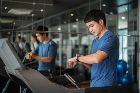 man running on treadmill and checking smart watch for performance at fitness gym exercise