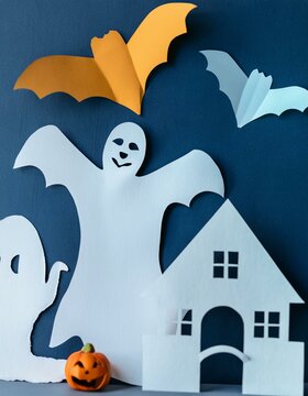 Whimsical ghost and bat cutouts with a small pumpkin on a dark blue background. Ideal for adding a playful touch to Halloween-themed greeting cards, flyers, and digital invitations.