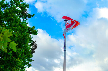 Canadian Flag Waving on Flagpole Against a Blue Sky with Trees and Clouds