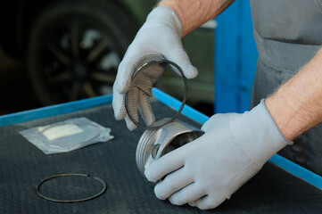 Car service. Engine repair. Checking the grooves of the piston rings before installation. An auto mechanic holds a piston and a piston ring in his hand.