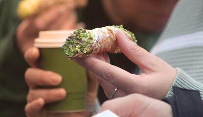 Pistachio Cannoli being held by a woman. She is also holding a take away coffee cup. Streetfood