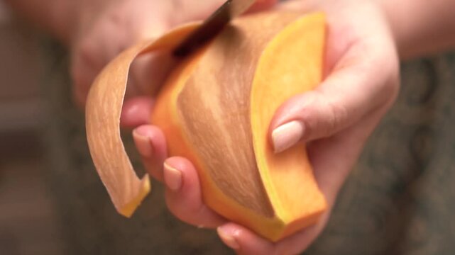A person is cutting a piece of orange squash with a knife. The squash is peeled and cut into slices.