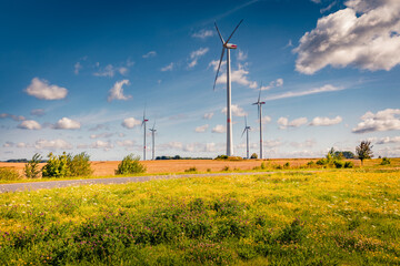 Electric turbines among a field of blooming yellow flowers. Pictueresque summer view ofgerman countryside. Ecology concept background.